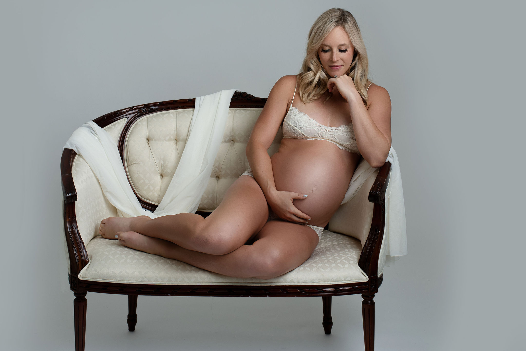 mom to be wrapped in a white fabric sitting on a cream couch cradling her bump Prenatal Yoga Tampa