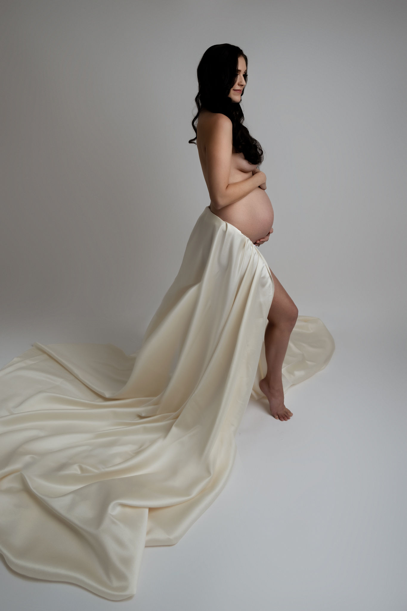 mother to be stands in a studio with a flowing dress