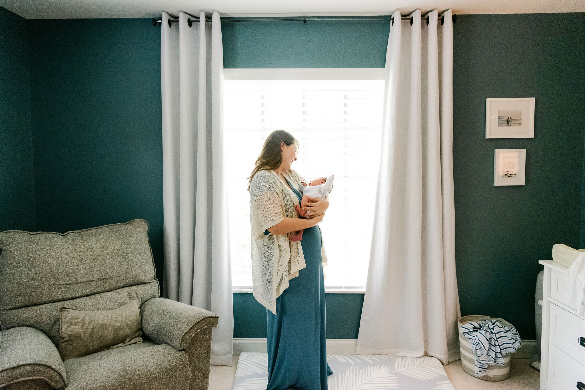 Mother stands in front of window holding her newborn in nursery