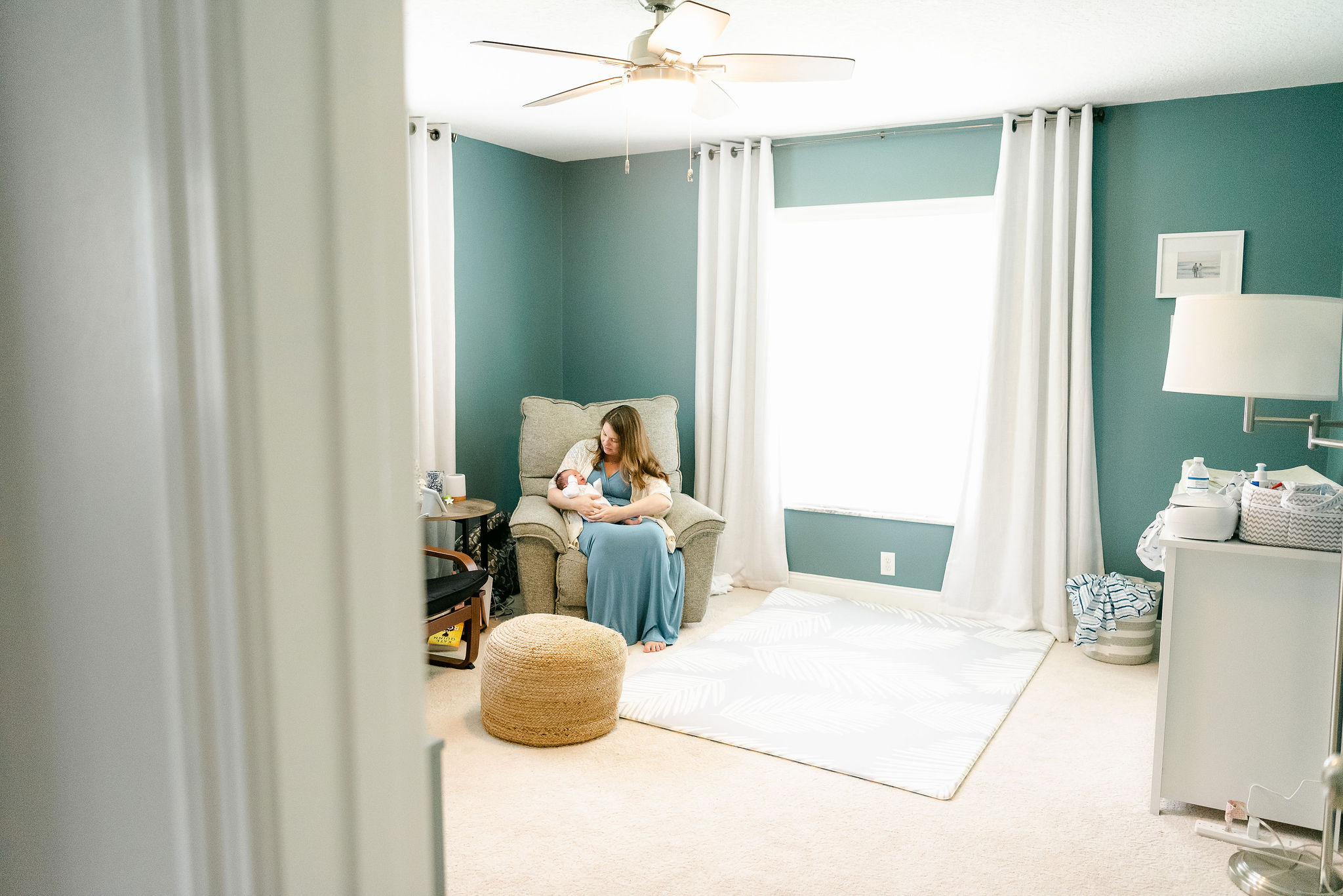 Mother in blue gown sits in nursery chair with newborn tampa doula