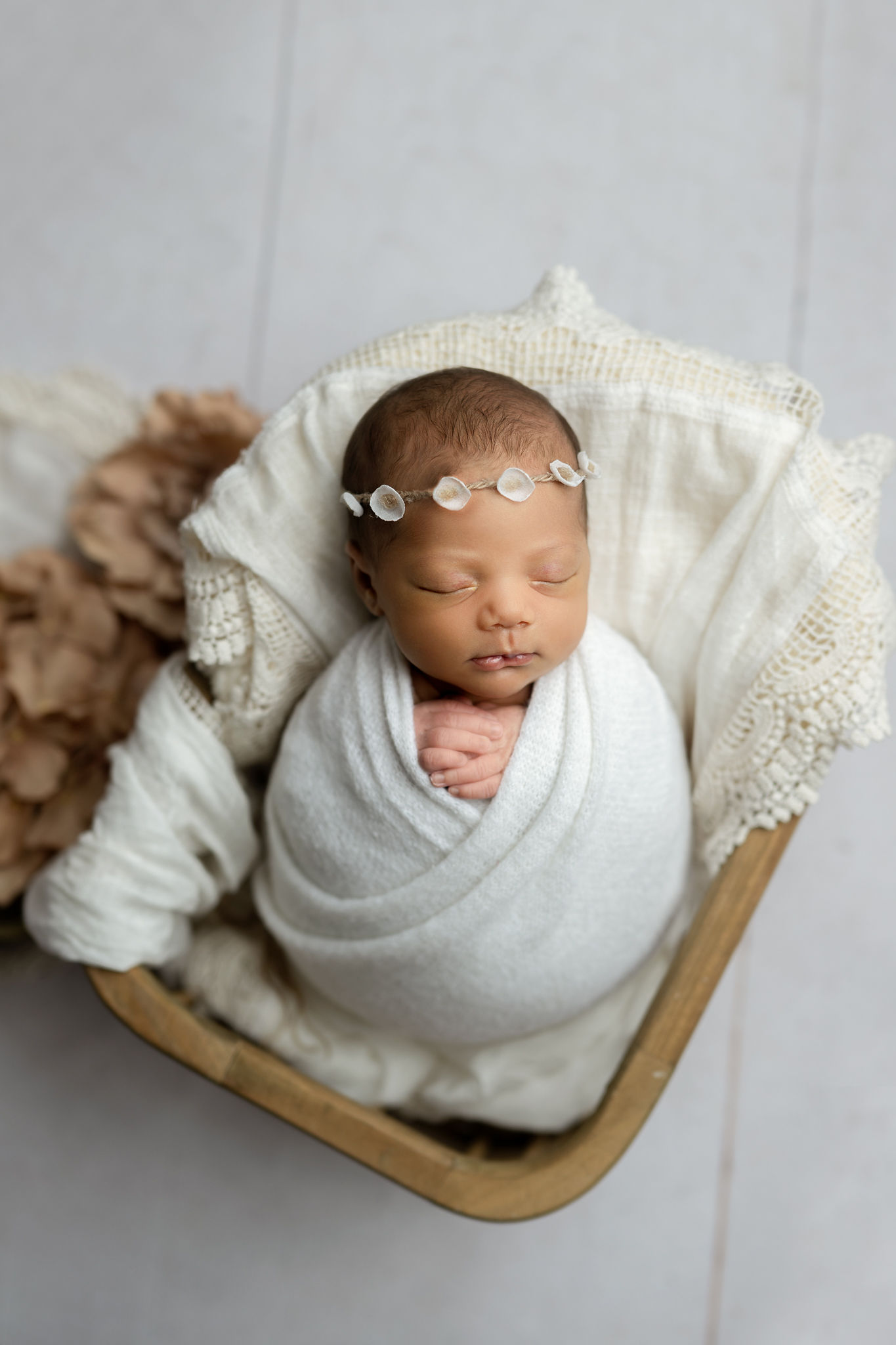 Newborn baby sleeps in a white swaddle positioned in a wooden basket