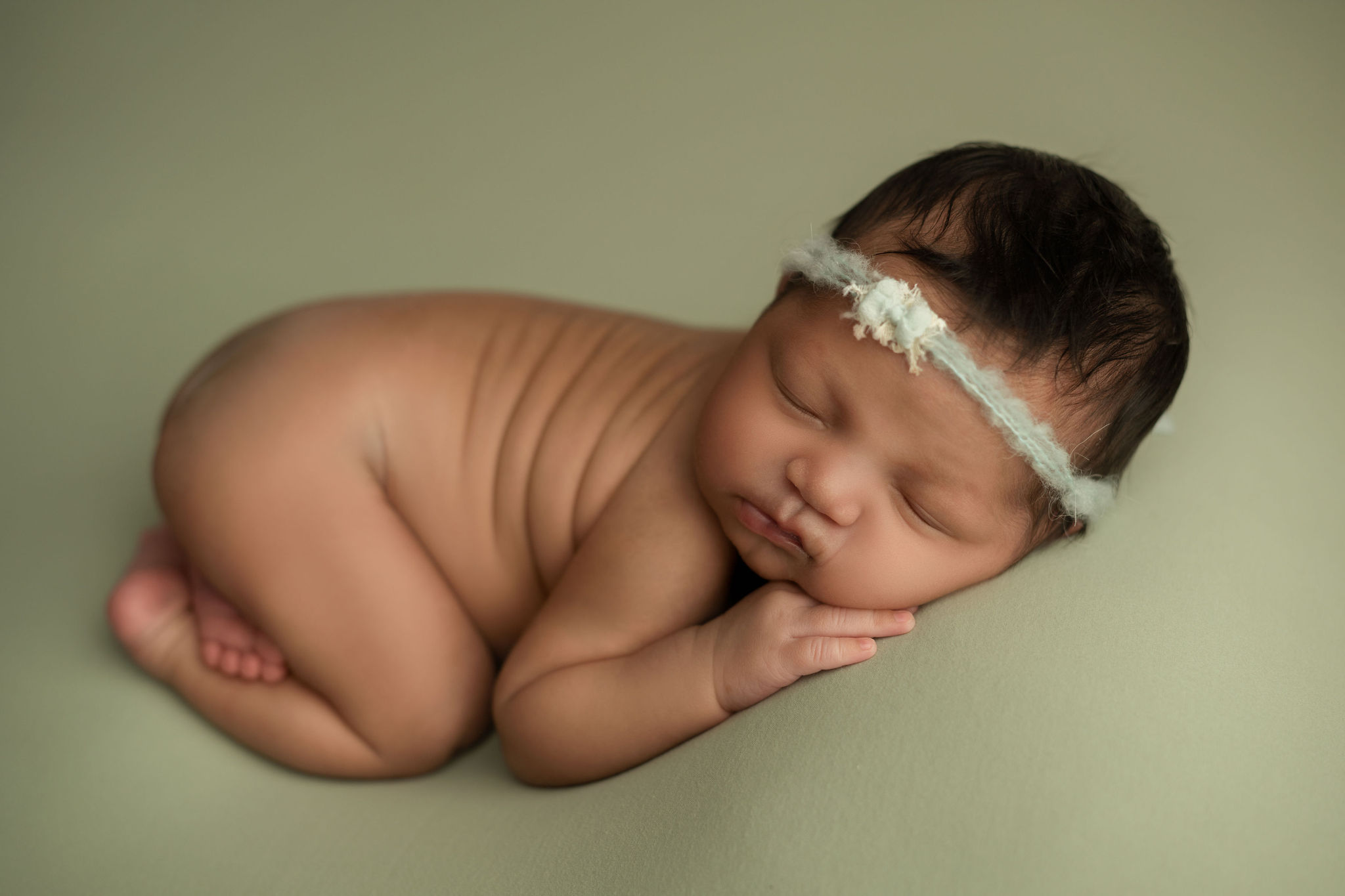 A newborn baby sleeps in the froggy pose wearing a green headband tampa baby boutique