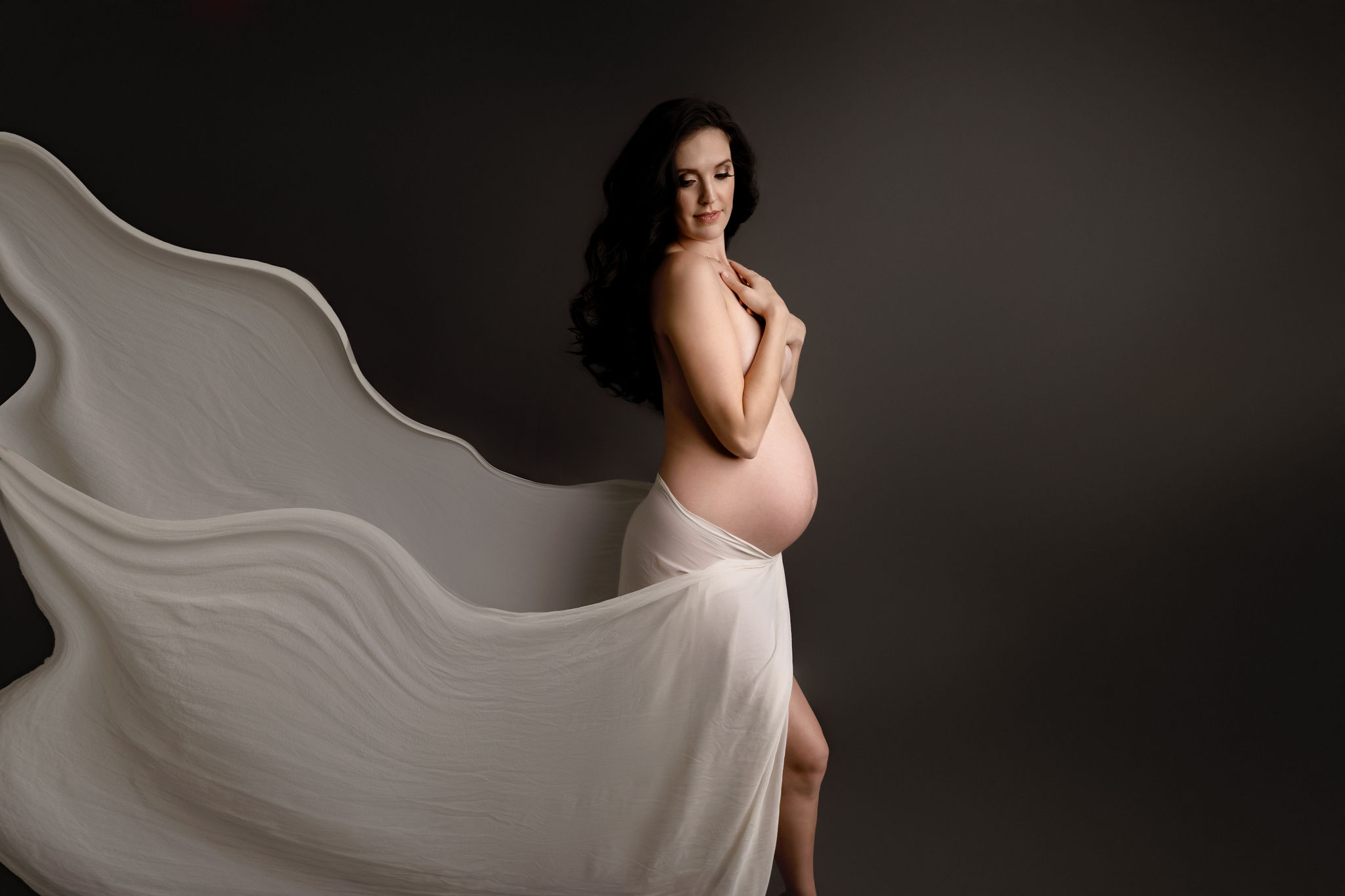 Pregnant woman wearing only a flowing dress stands in a studio covering with her hands tampa ultrasound