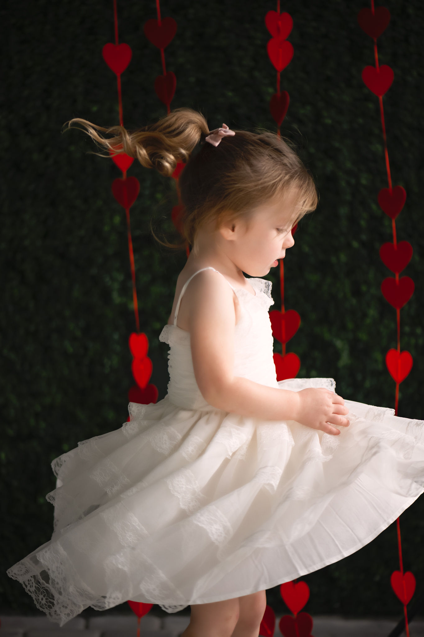 A young girl in a white lace dress plays and spins in a studio with red hearts hanging behind her tampa toy stores