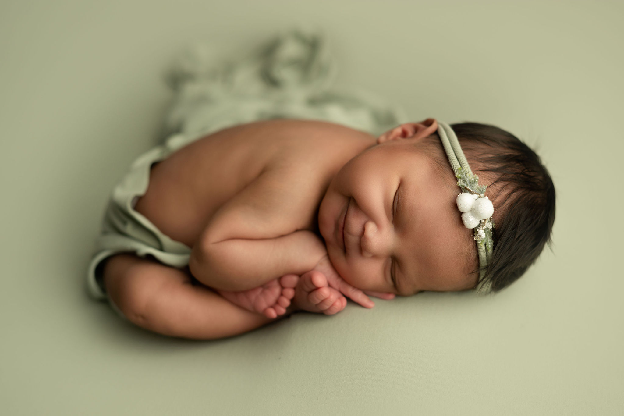 A newborn baby smiles in her sleep while wrapped in a green blanket in due season birth center