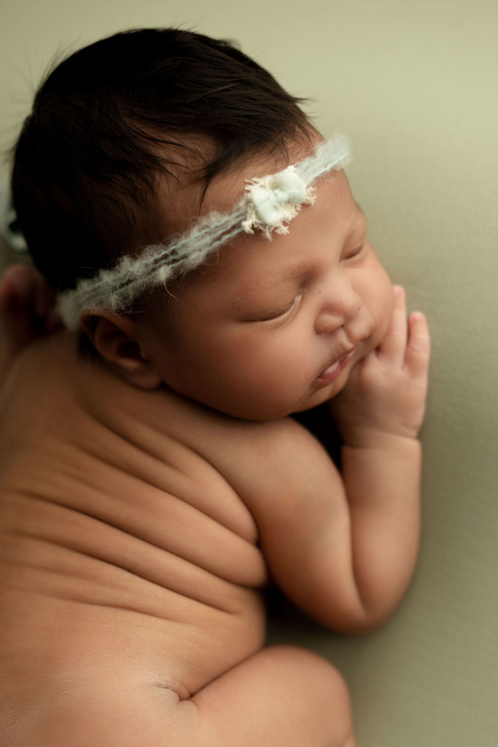 A newborn baby sleeps on its tummy wearing only a furry headband in due season birth center