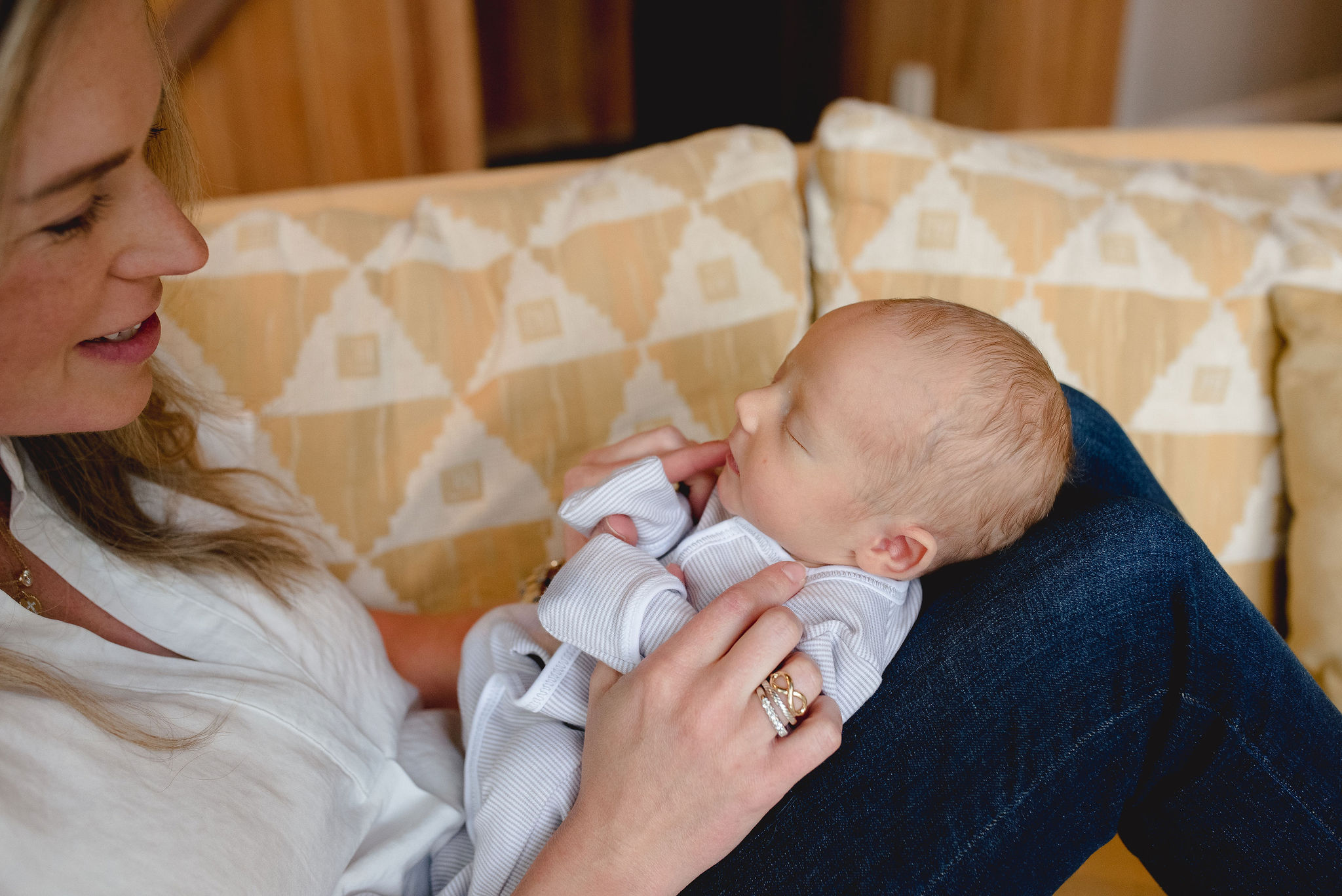 A newborn baby sleeps on mom's lap while they sit on a couch