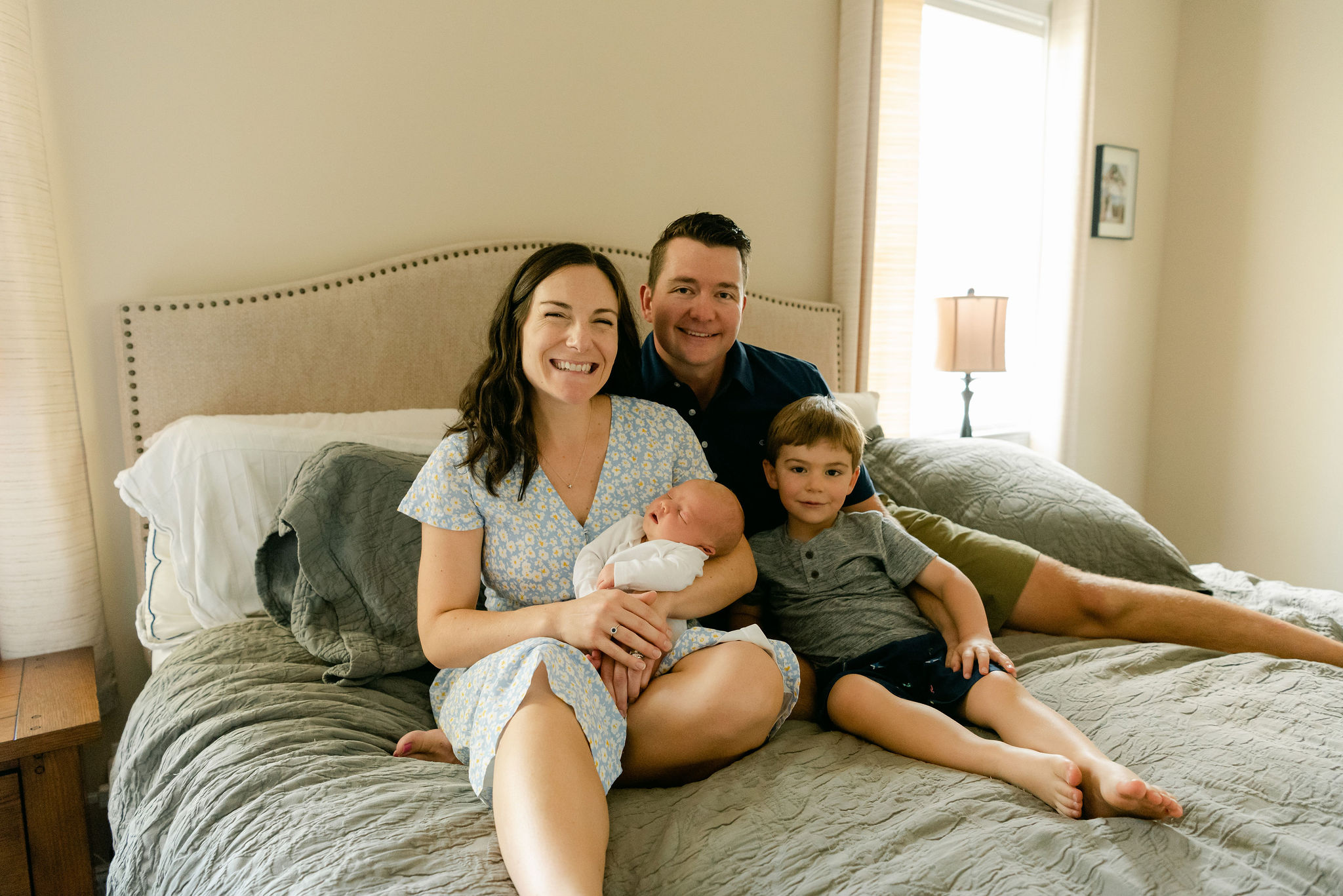 A family of four sit on a green bed with their newborn baby in mom's arms silly dilly tot spot